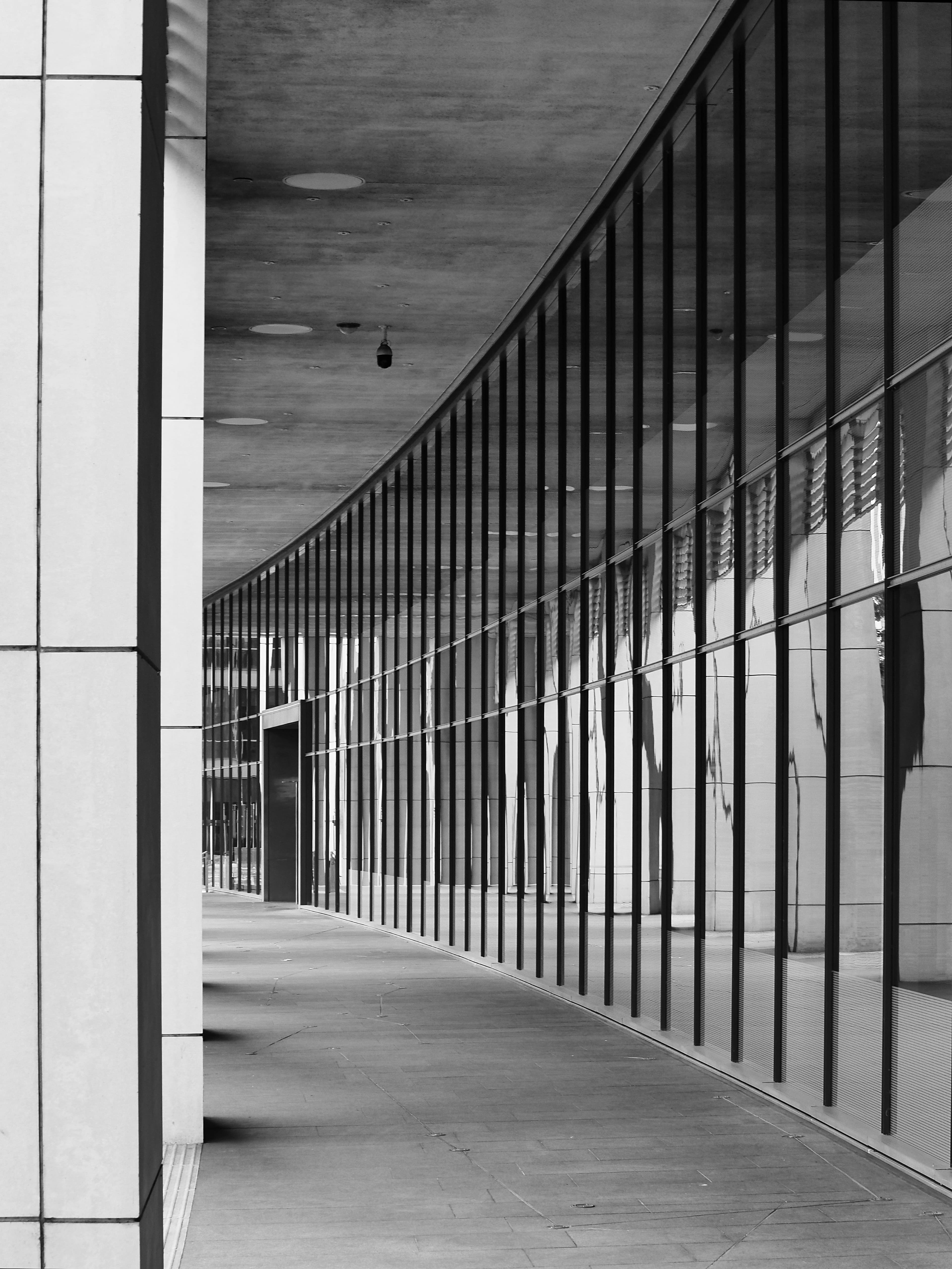 Corredor arquitetônico moderno em preto e branco, com estrutura de vidro, concreto e linhas verticais em perspectiva